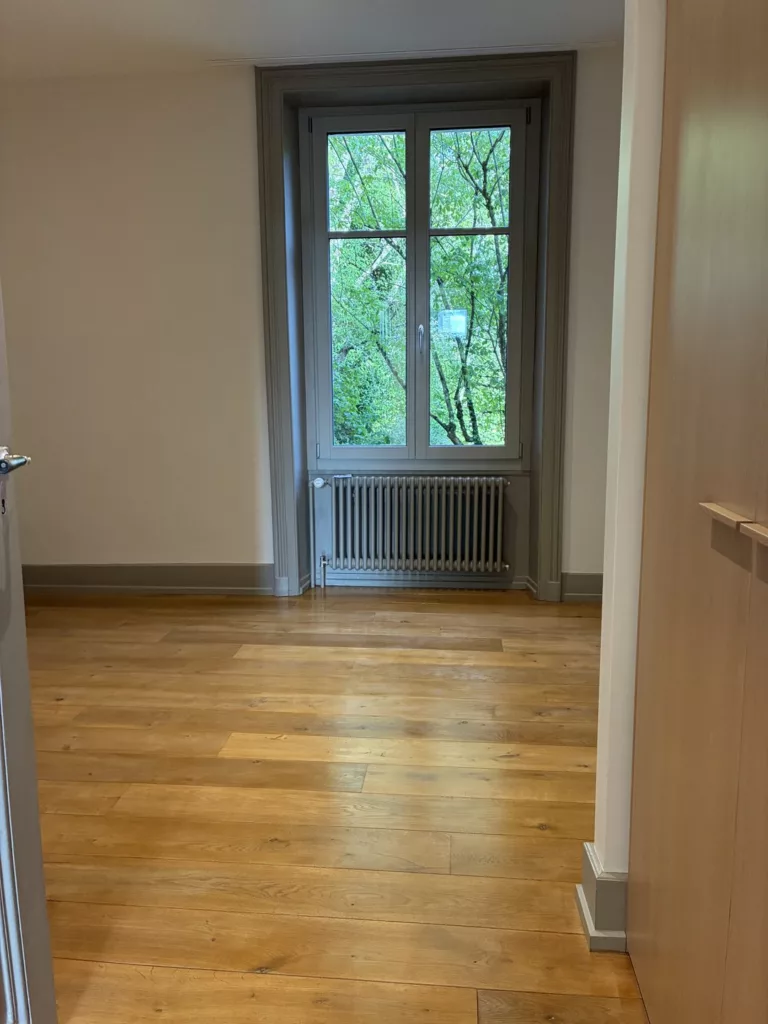 Chambre vide avec parquet et radiateur en fonte à Montricher, avant remise du logement